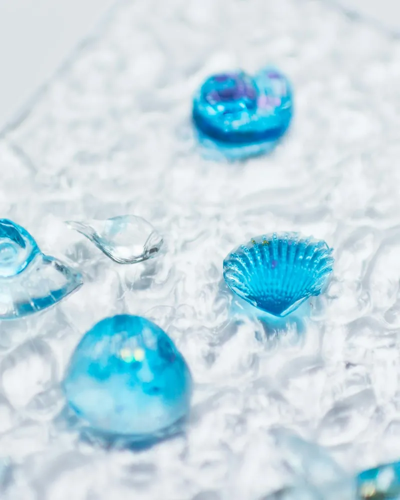 Pormenor de peças de vidro azul em forma de concha, gota e esfera sobre vidro transparente de superfície ondulada