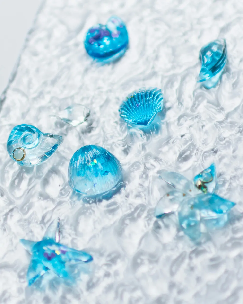 Placa de vidro transparente com textura ondulada, com pequenas peças de vidro azul em forma de concha e gota fundidas à superfície